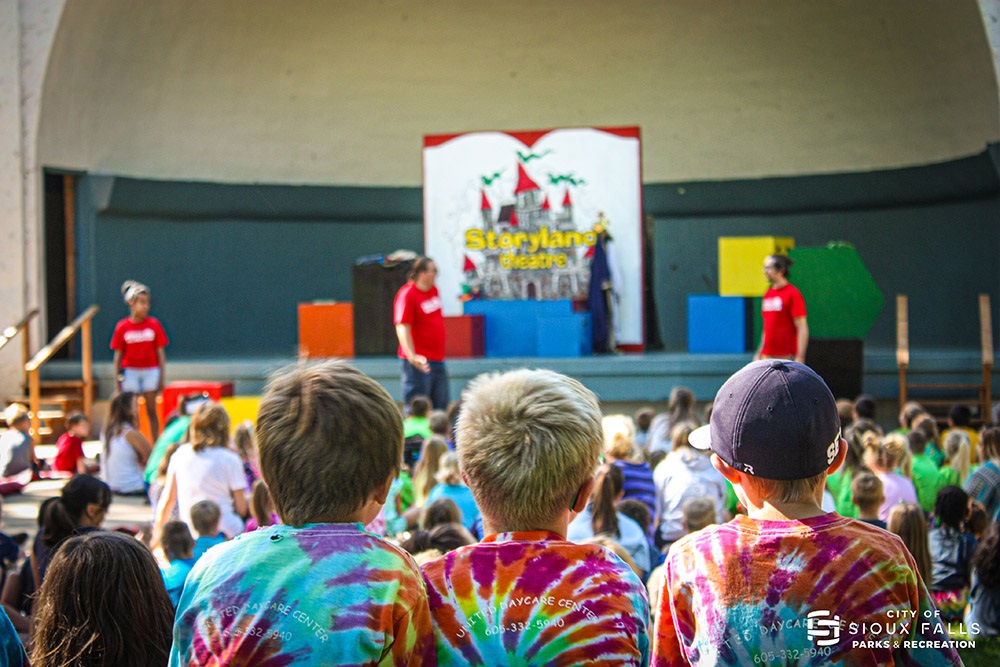 three children wearing tie dye shirts watching childrens storyland theatre