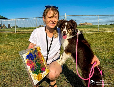 Dog smiling with owner and painting made by the dog