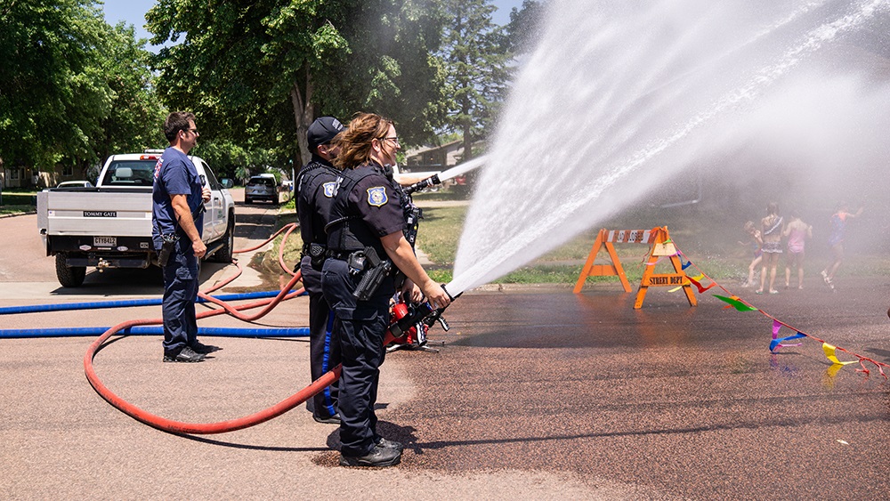 Police officers holding the fire hose spraying the children at the hydrant block party 