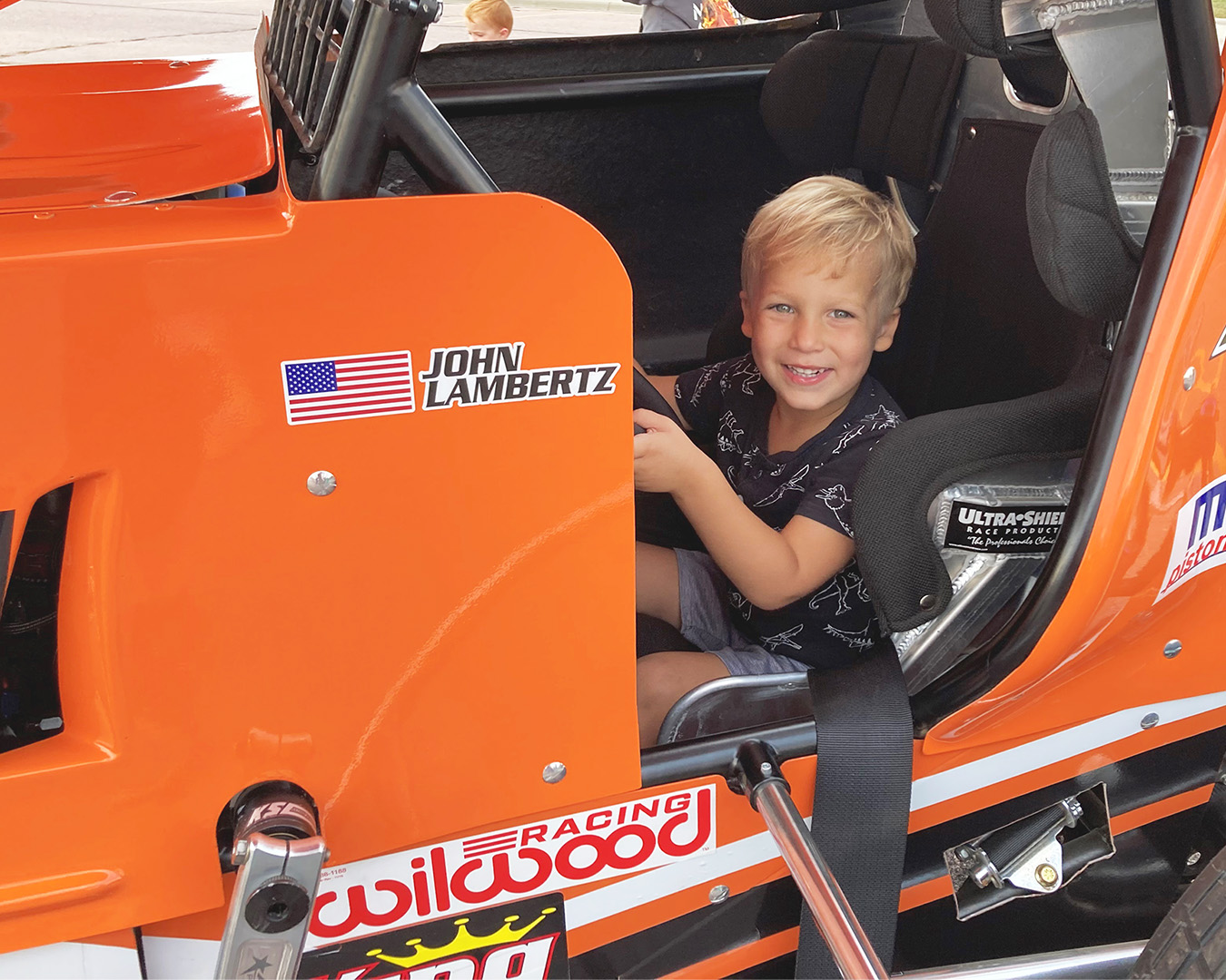 A child sitting in the driver's seat of a race car, smiling at the camera.